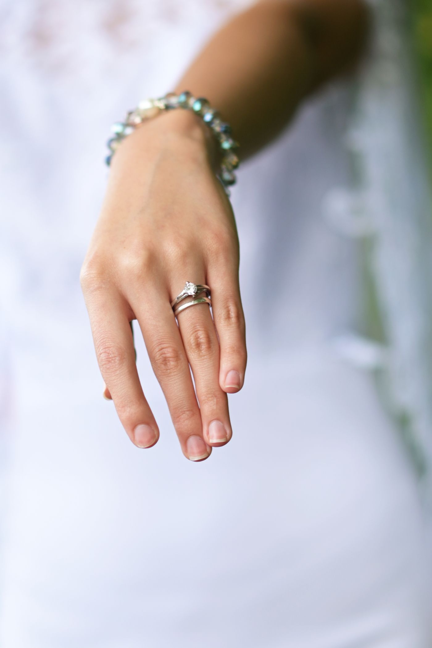 A woman's hand wearing an engagement ring against a white dress