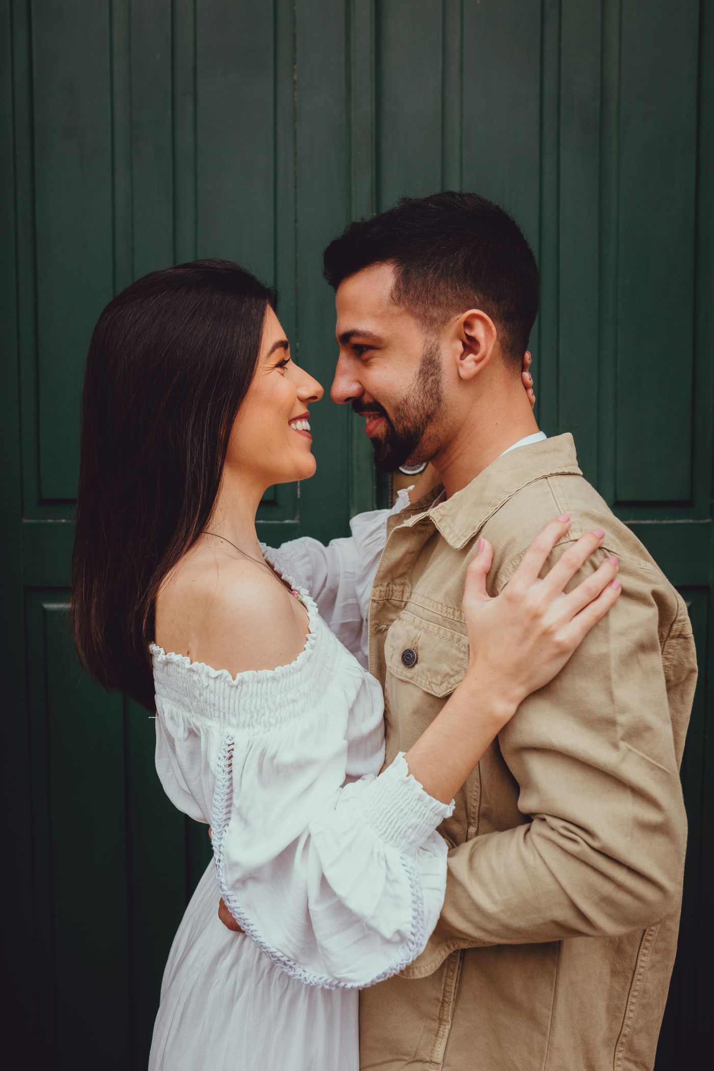 A couple standing close together in front of a green door, her in white, him in tan
