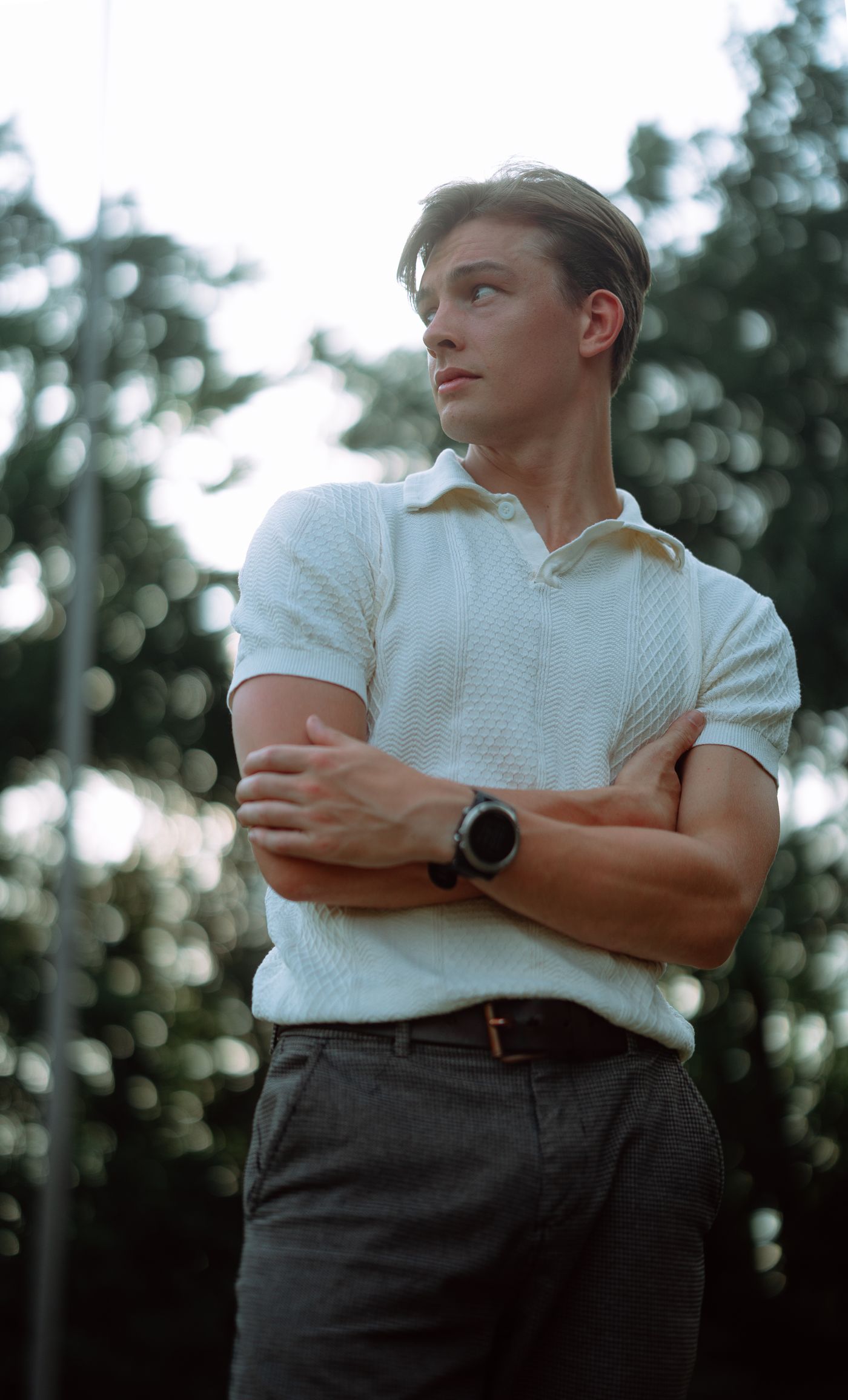 A man in a fitted white knit polo, tailored trousers and a wristwatch